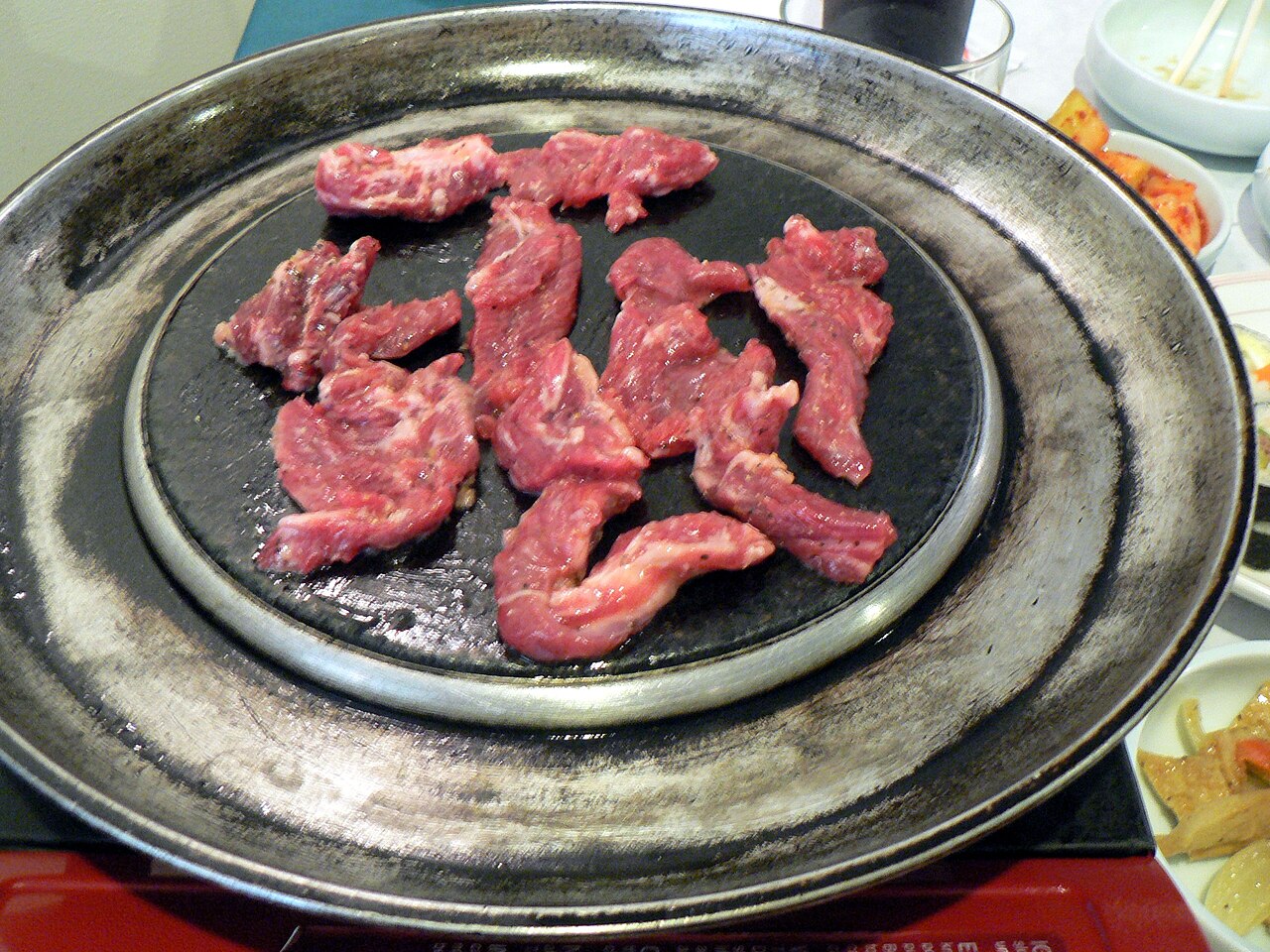 Raw boneless galbisal pieces on a black grill plate