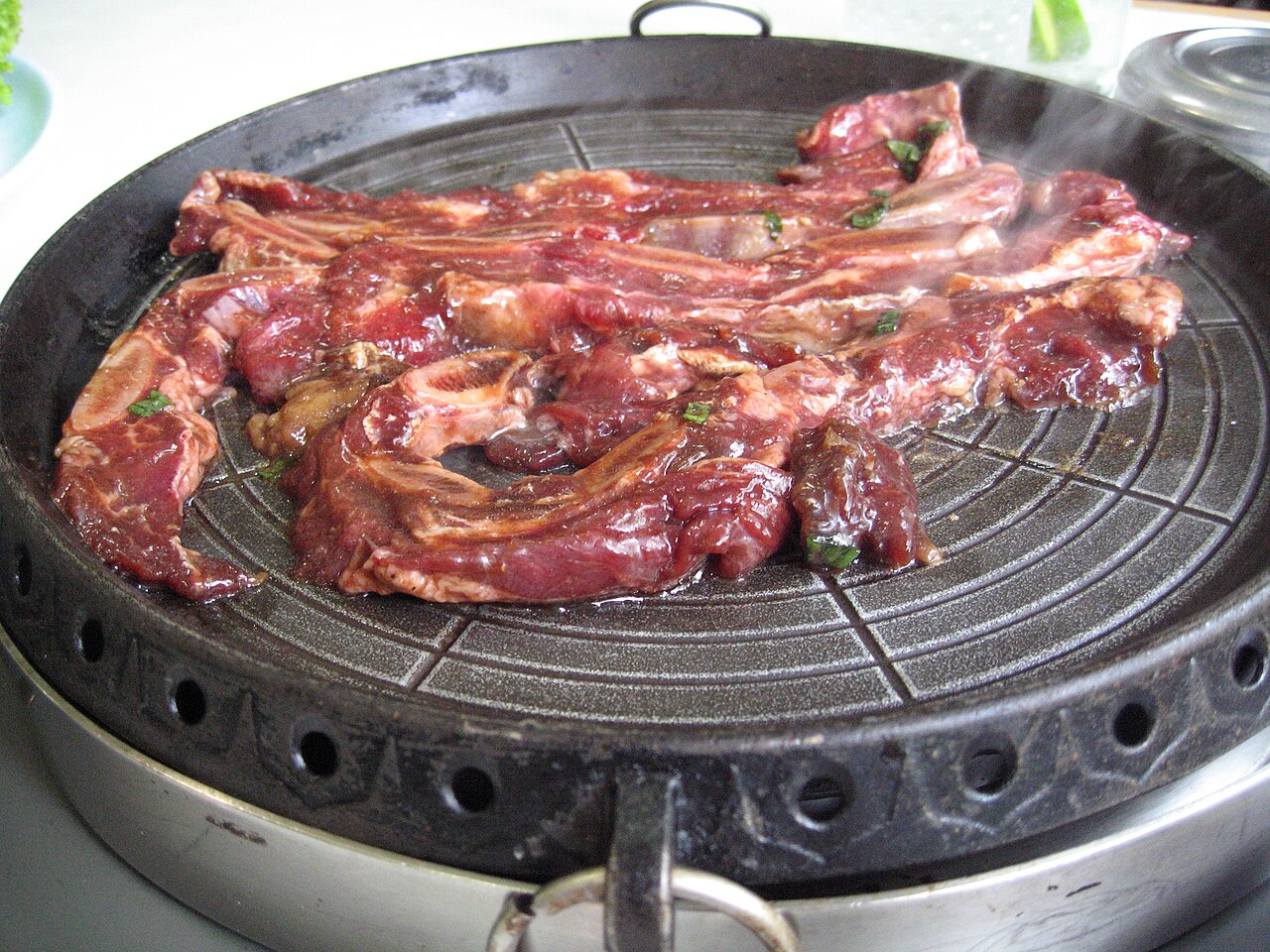 Thin cross-cut LA-style ribs with bones on a round table grill
