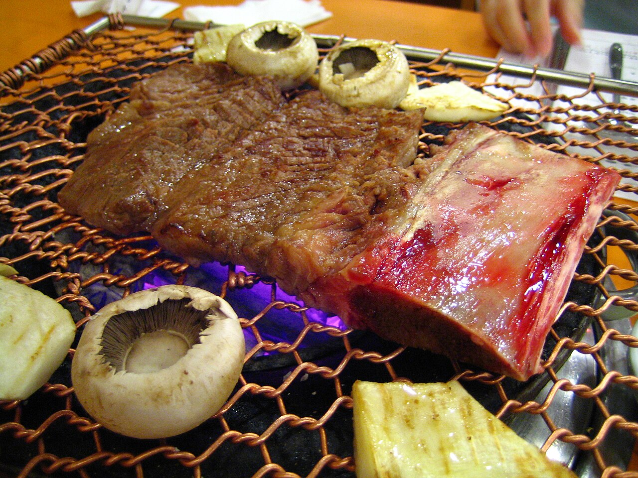 A thick beef short rib on a charcoal grill with mushrooms