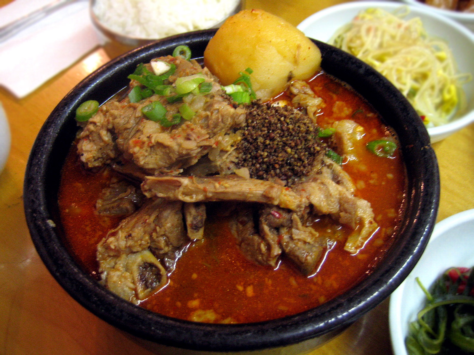 Gamjatang, a red pork bone stew with a potato on top and scallions