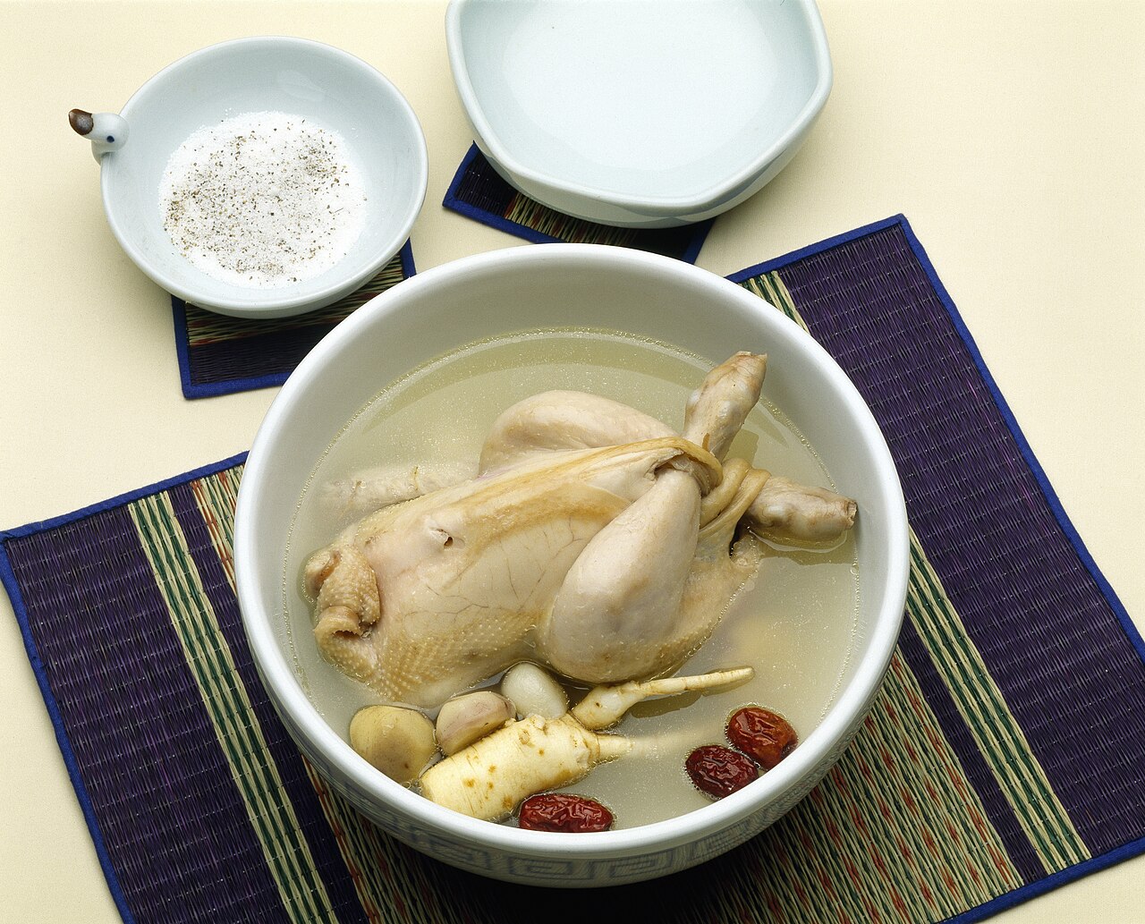 Samgyetang, a whole young chicken in broth with ginseng and jujubes in a white bowl