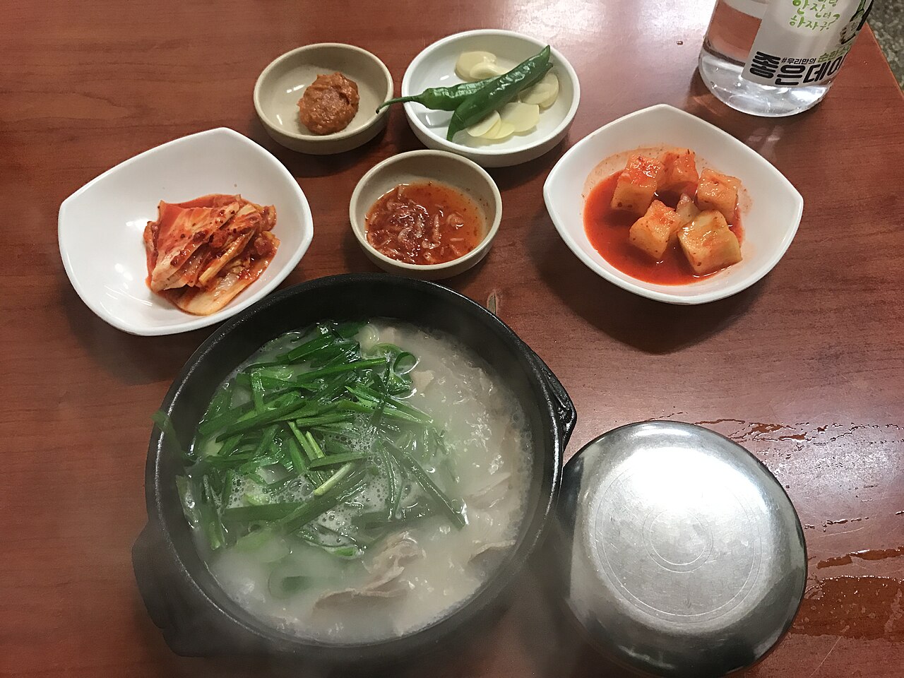 A bowl of pork gukbap with chives, served with kimchi, pickled radish and other side dishes