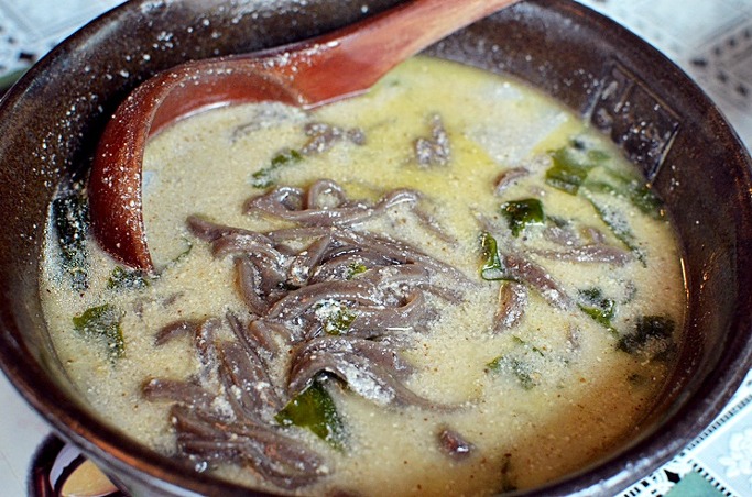 A bowl of deulkkae kalguksu with dark noodles and a creamy broth of ground perilla seeds