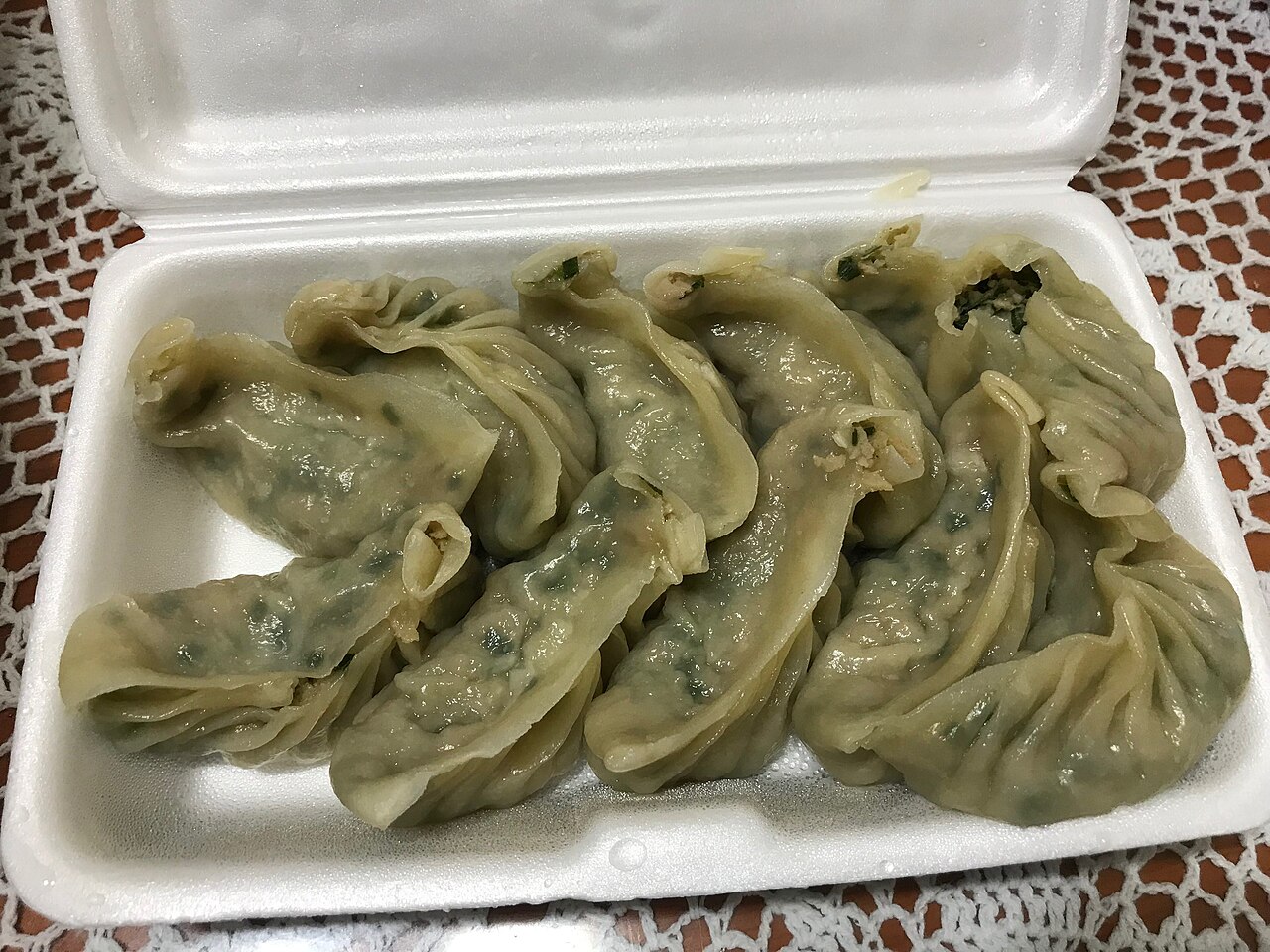 Steamed gogi-mandu with a thin green-tinged wrapper, filled with minced meat and chives, in a takeaway box