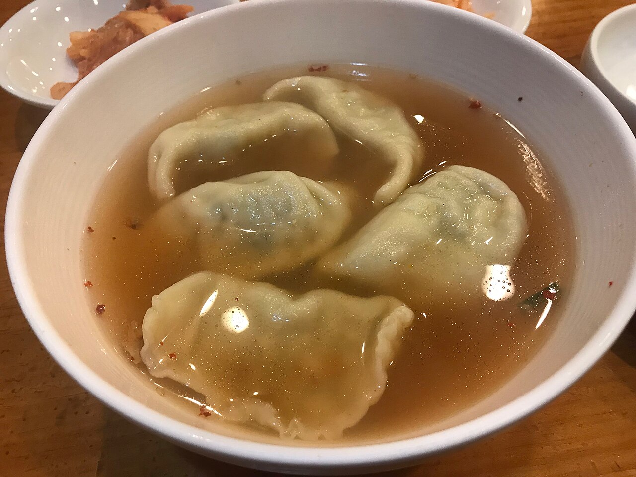 A white bowl of manduguk, with four dumplings in a clear light-brown broth