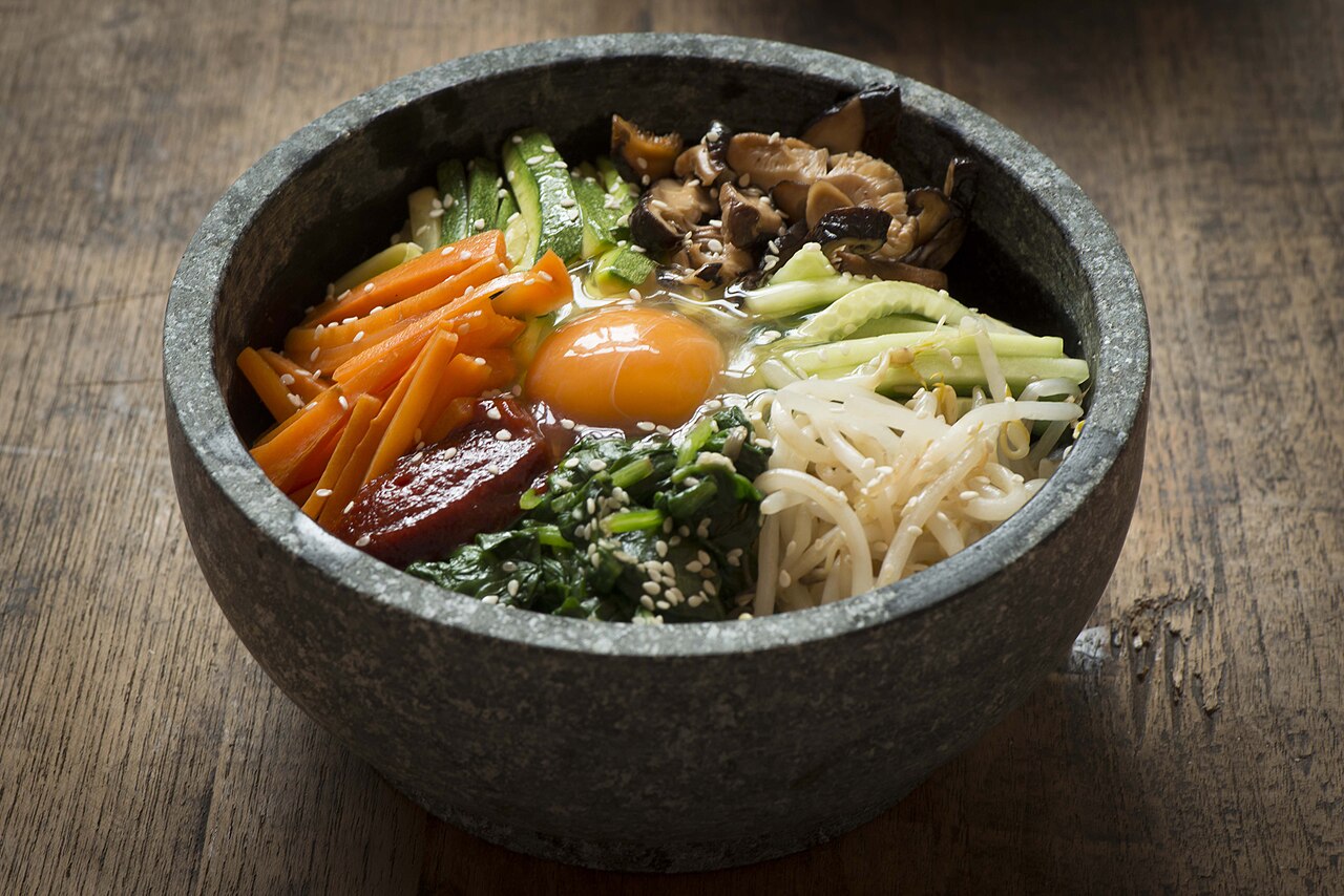 A stone bowl of bibimbap with carrots, zucchini, mushrooms, spinach, bean sprouts and an egg yolk