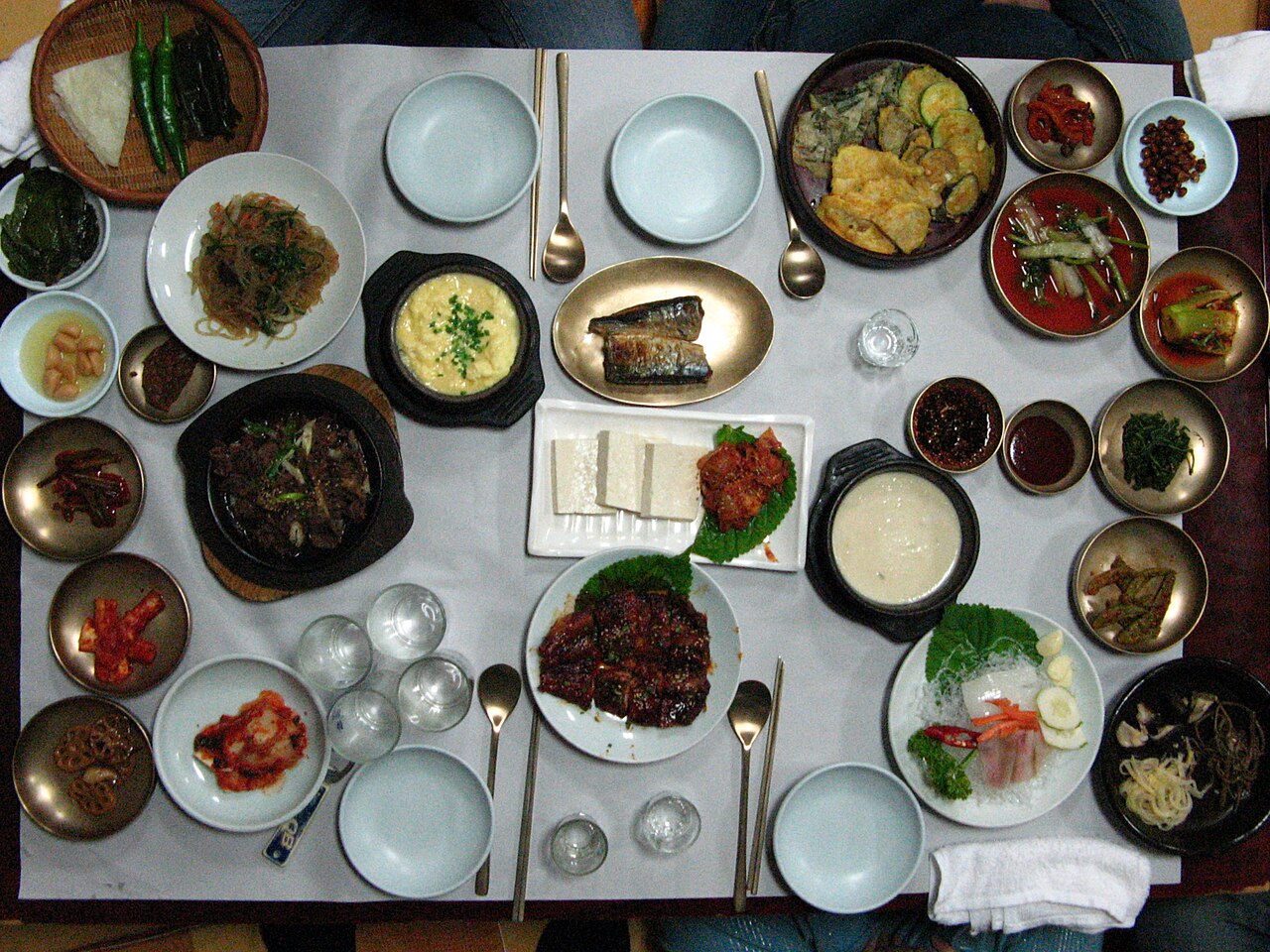 An overhead view of a hanjeongsik table covered with many dishes: grilled fish, meat, egg, vegetables, kimchi and a hot pot