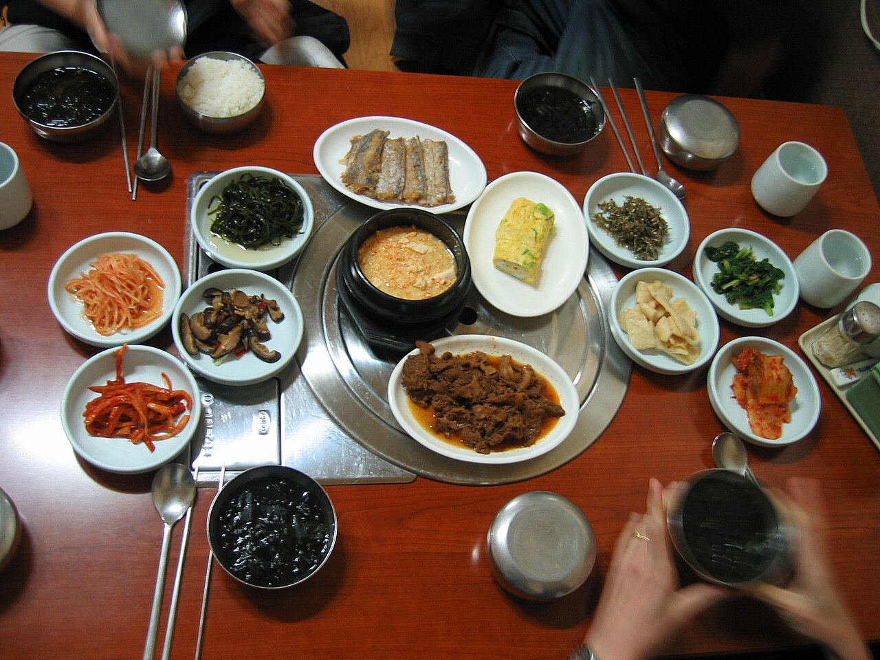 A baekban table with rice, a soy-paste stew, grilled fish, rolled egg, meat and many small side dishes