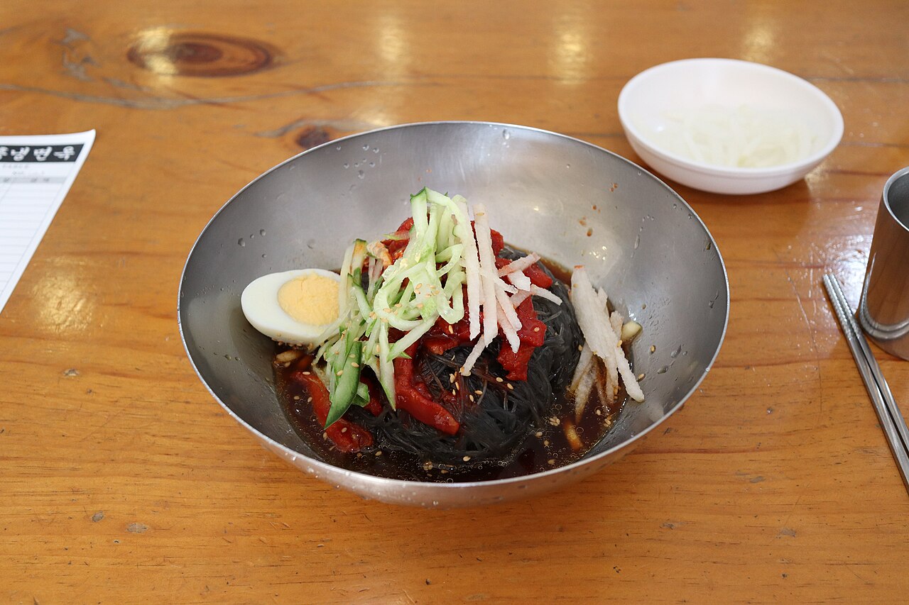 Hamheung-style naengmyeon with dark noodles, red sauce, cucumber, pear and egg