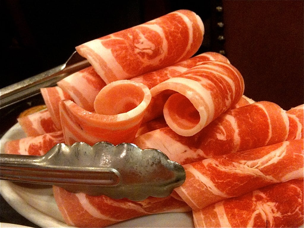 Paper-thin rolled slices of pork belly on a plate with tongs