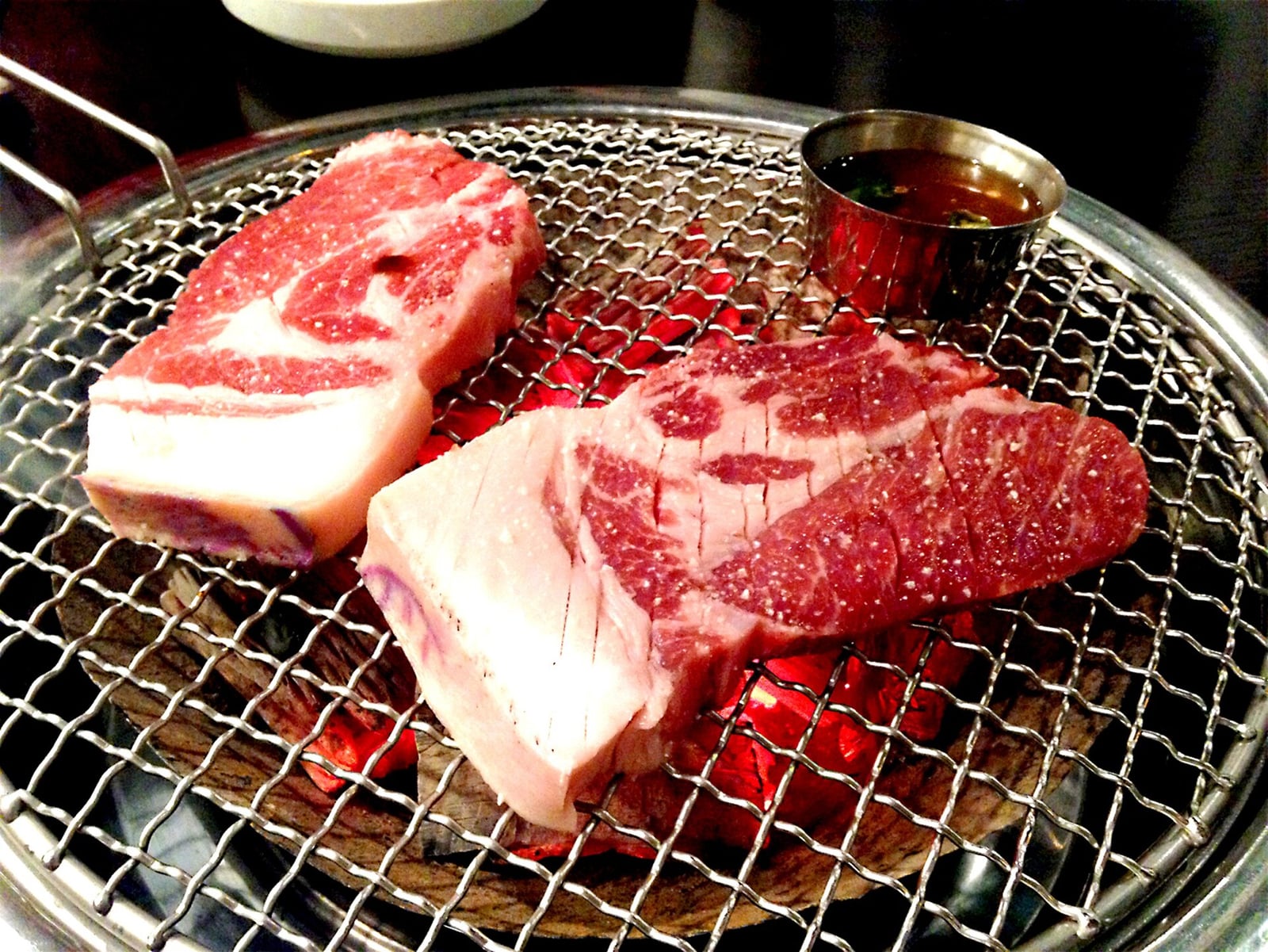 Thick cuts of pork with shallow knife scores resting on a charcoal grill