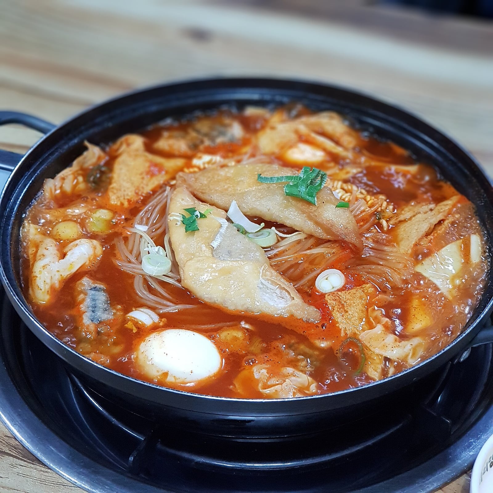 A pot of jeukseok tteokbokki with fish cake, glass noodles and egg over a table burner