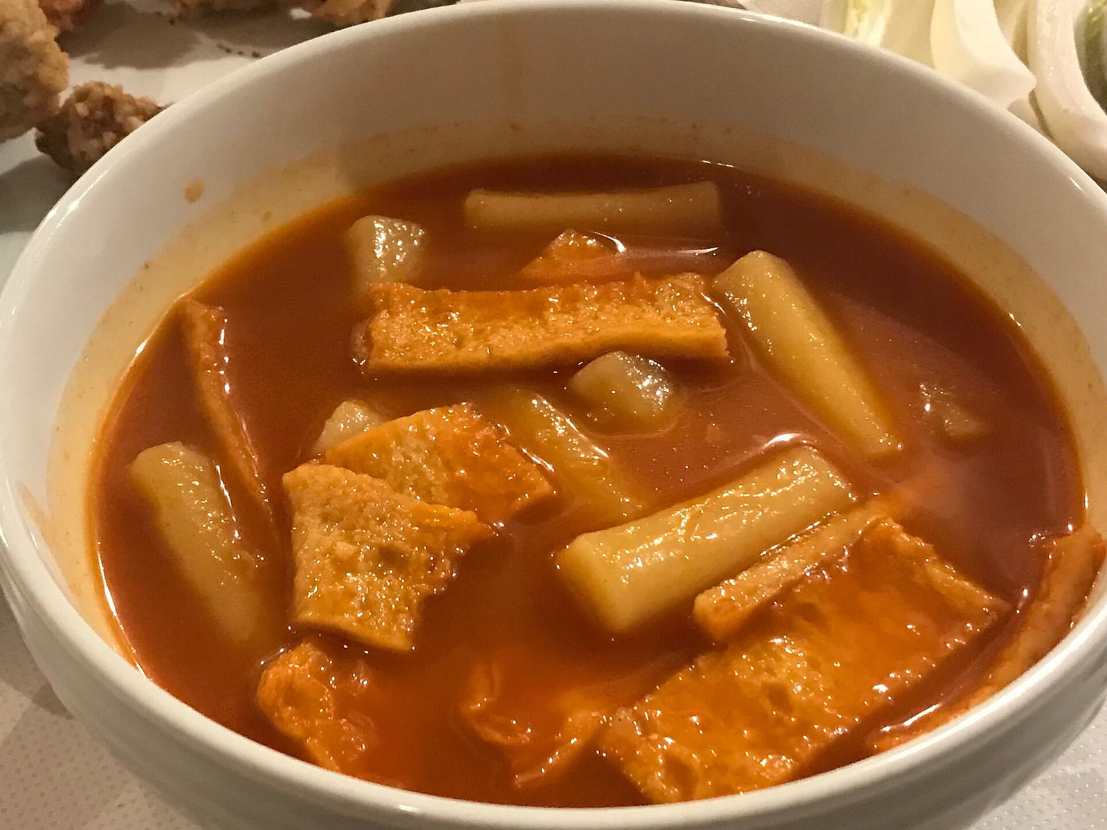 A bowl of soupy tteokbokki with rice cakes and fish cake in red broth